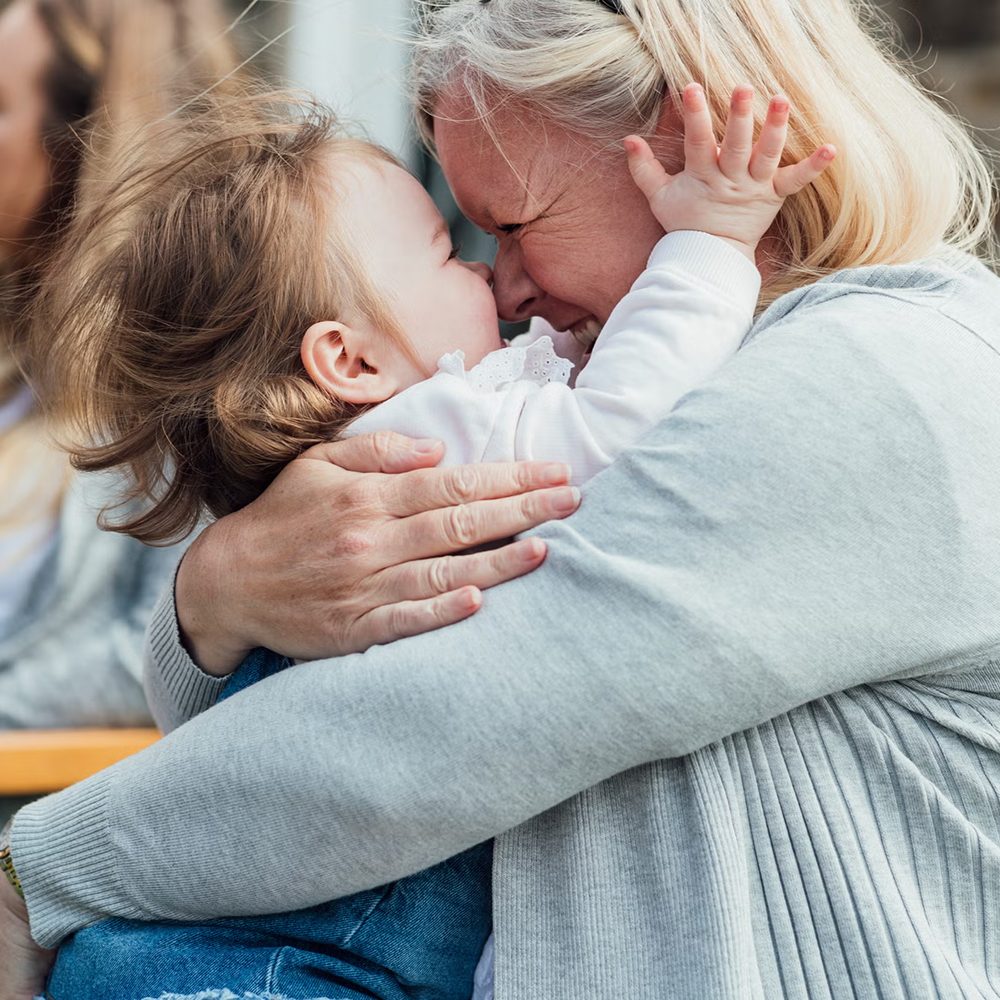 Joslin Rhodes - Woman happily lifting a smiling child, sharing a joyful moment together.