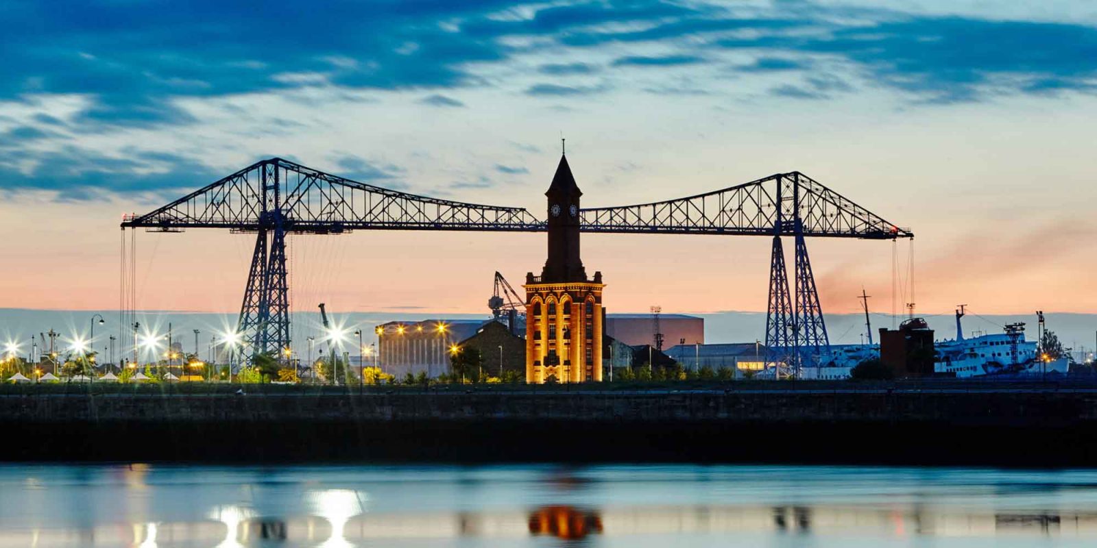 Joslin Rhodes - The Transporter Bridge at dusk with the River Tees flowing beneath and a colourful evening sky in the background.
