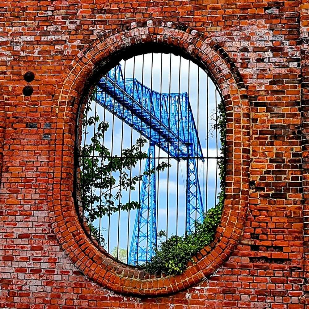 Joslin Rhodes - Striking view of Middlesbrough’s iconic Transporter Bridge framed through a weathered brick wall, capturing the town’s industrial heritage.