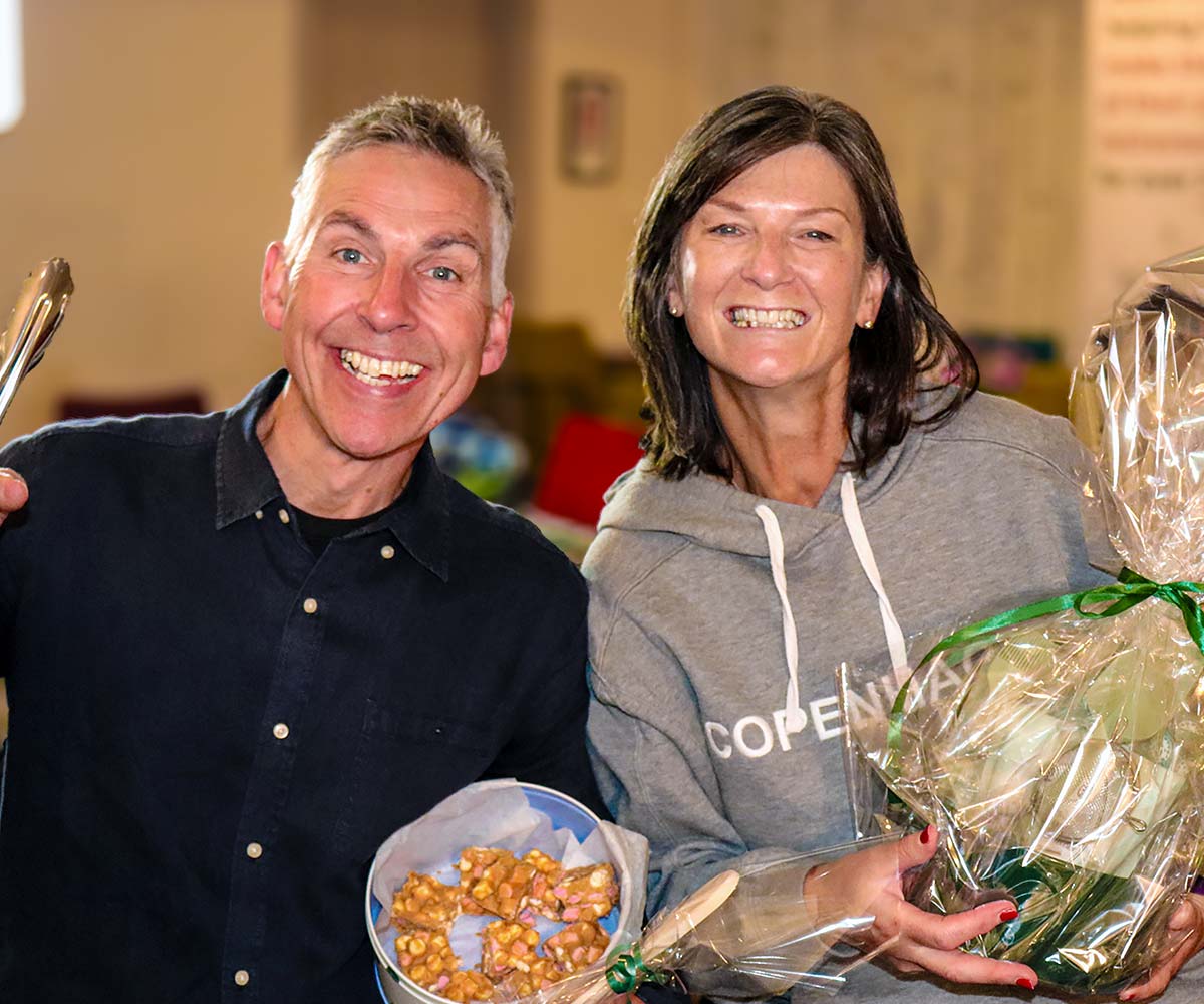 Joslin Rhodes - Clients smiling at a client event while holding their winning prizes; he has baked treats, and she has a hamper.