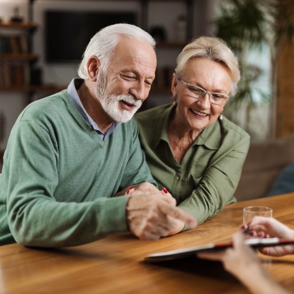 Joslin Rhodes - Couple sitting in their lounge, smiling and looking at their retirement plan together.