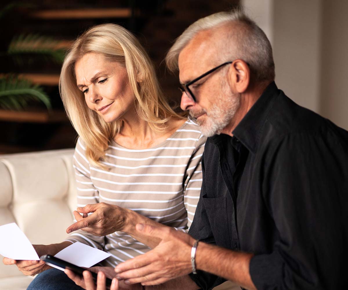 Joslin Rhodes - Middle-aged couple sitting on their sofa, reviewing documents together.