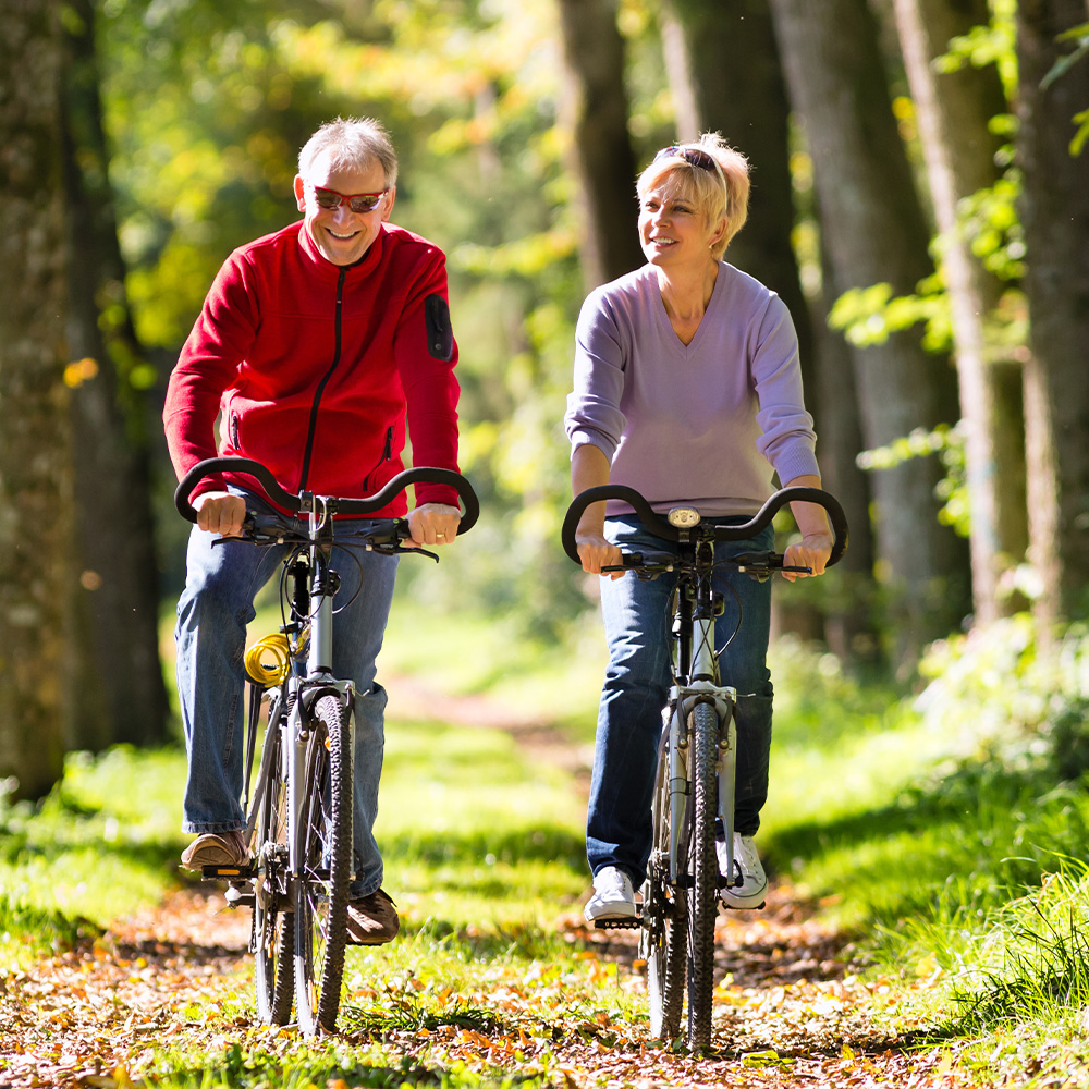 Joslin Rhodes - Retired couple cycling together through a wooded trail.