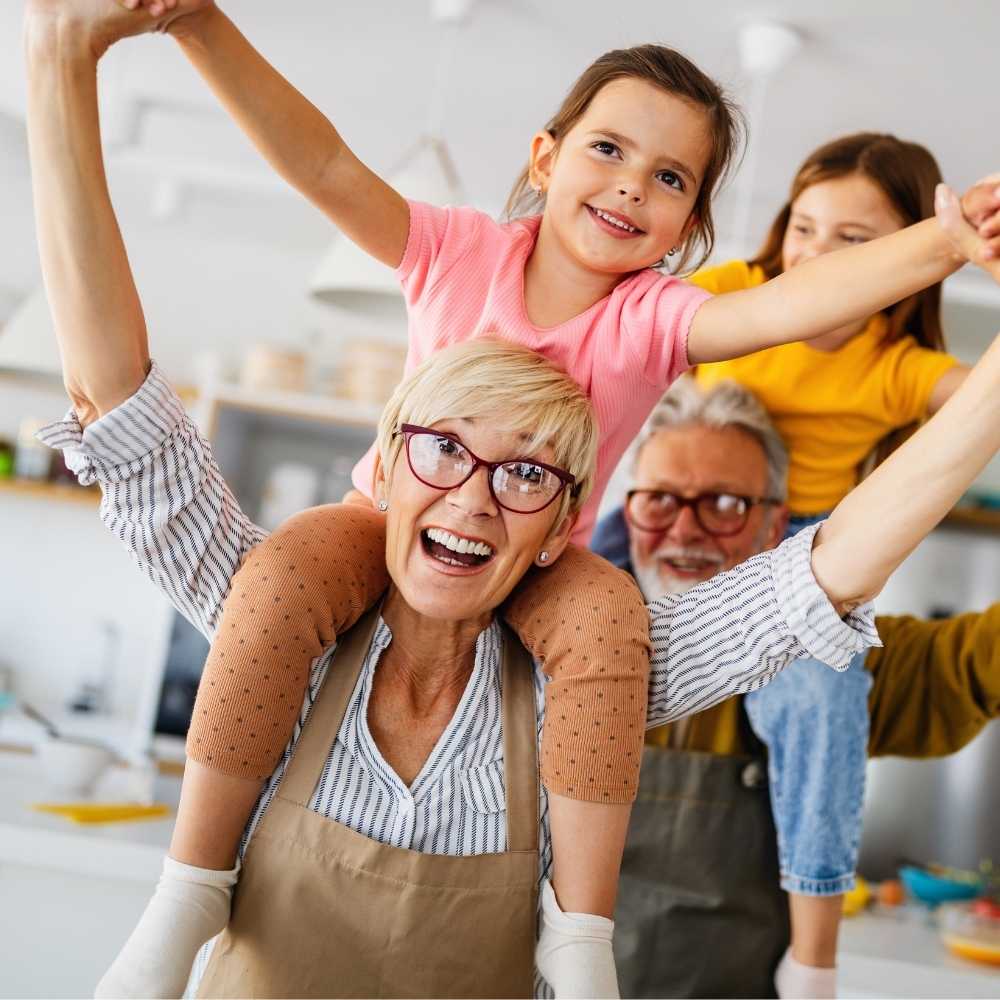 Joslin Rhodes - Grandparents joyfully lifting their grandchildren in a kitchen, all smiling and happy.