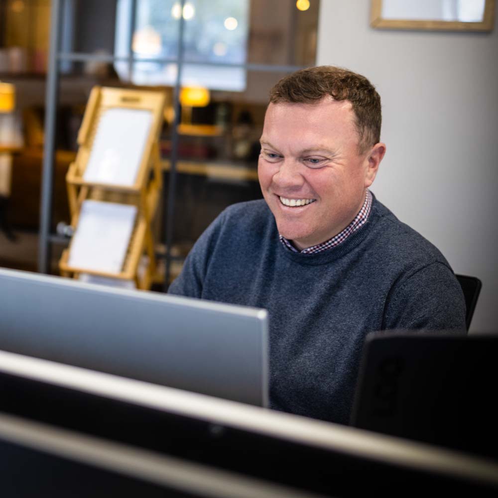Joslin Rhodes Financial Planner smiling while working on a laptop in a professional office setting.