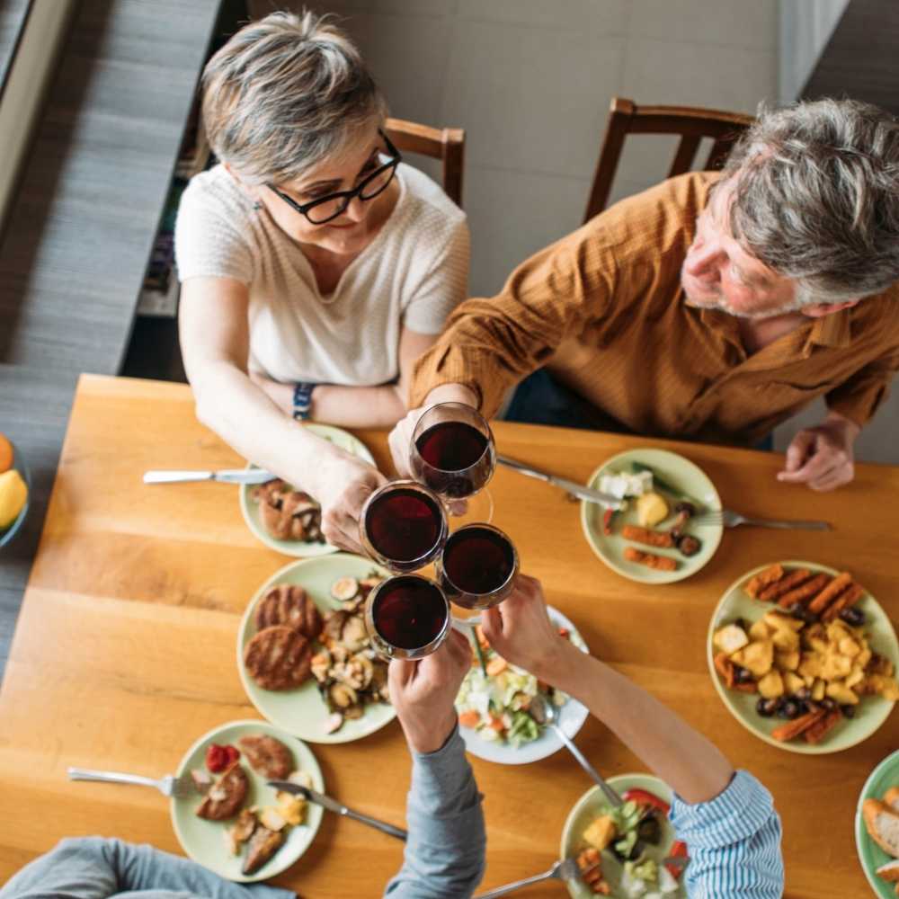 Joslin Rhodes - Friends toasting over a hearty meal, celebrating connection and joy in retirement—living life to the full.