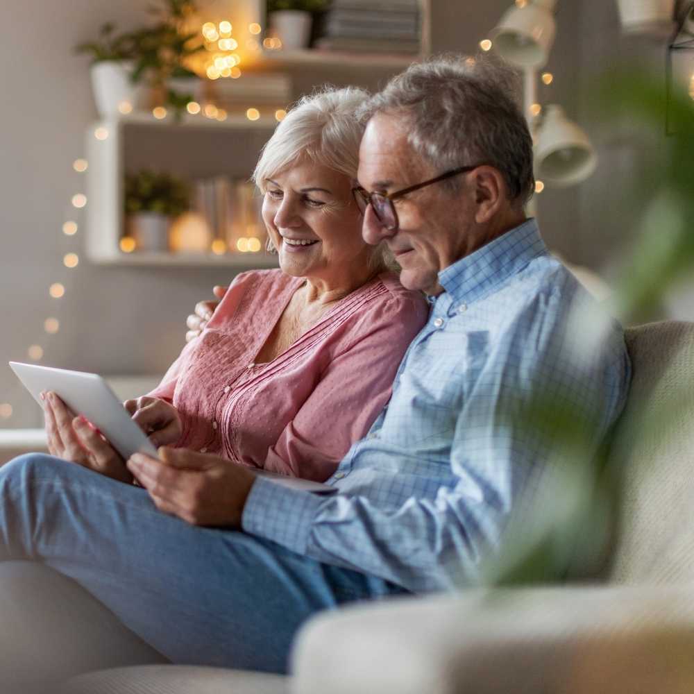 Joslin Rhodes - Image of a retired couple smiling at their iPad in in their living room.